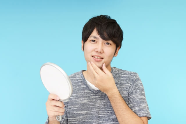 鏡を持ち顔を触る男性
